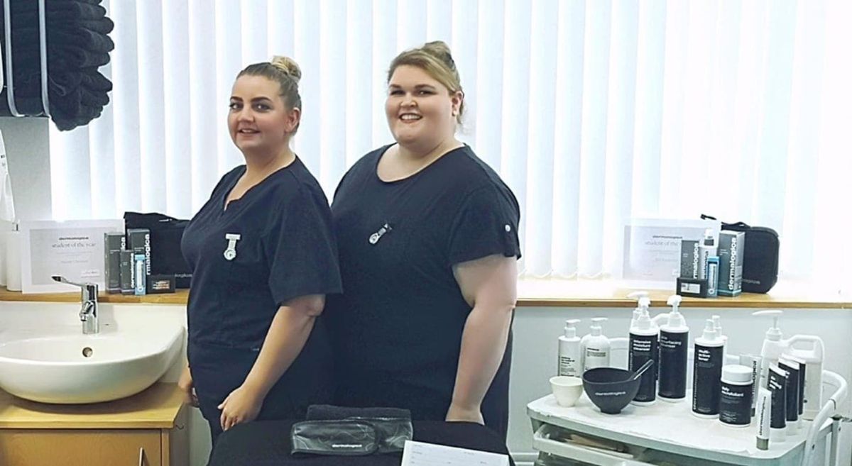 Two female students in a spa/beauty setting with a beauty products and a sink